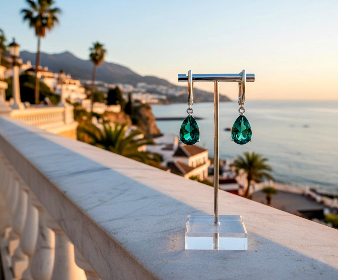 Green teardrop earrings on a stand with a scenic background of mountains and sea.