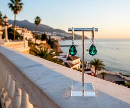Green teardrop earrings on a stand with a scenic background of mountains and sea.