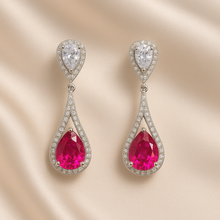 Long ruby teardrop earrings with white quartz halo on satin background