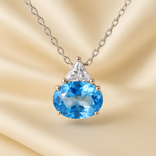 Oval blue topaz and triangular white quartz necklace on cream satin background