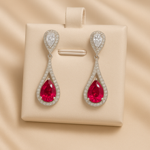 Long ruby teardrop earrings with white quartz halo on satin background