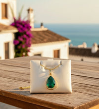 Jewelry box with a green teardrop pendant on a wooden surface with a scenic background.