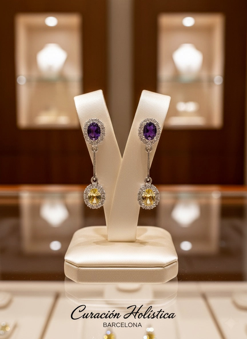 Pair of earrings with purple gemstones on a white stand, with 'Curacion Holistica Barcelona' branding.