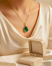 Gold necklace with a green pendant on a mannequin, next to an open jewelry box on a white fabric background.