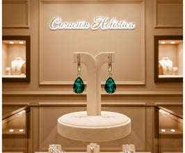 Green teardrop earrings on a display stand with 'Caracterótica' branding in the background.