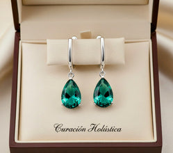 Green teardrop earrings in a jewelry box with 'Curacion Holistica' branding.