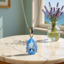 Blue teardrop pendant necklace on a marble surface with a vase of flowers in the background