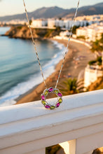 Necklace with a colorful pendant on a railing overlooking a beach and cityscape.