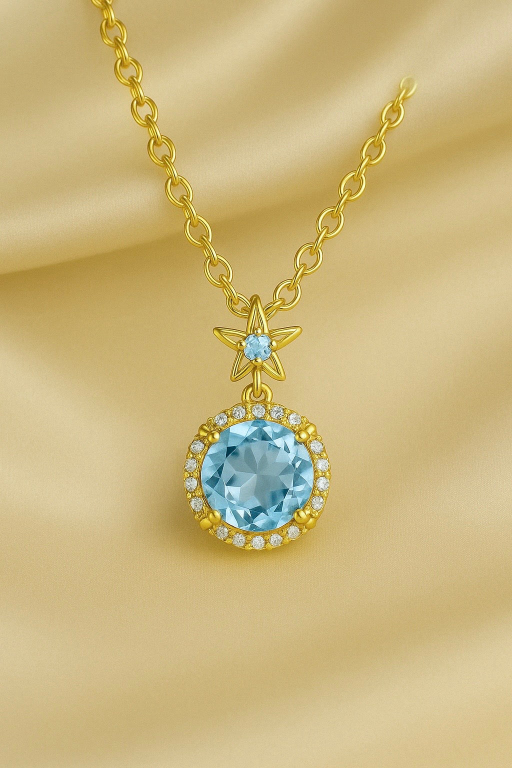 “Elegant gold-plated sterling silver necklace featuring a radiant aquamarine gemstone surrounded by a delicate halo of sparkling stones, displayed on a luxurious cream satin background.”