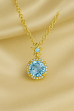 “Elegant gold-plated sterling silver necklace featuring a radiant aquamarine gemstone surrounded by a delicate halo of sparkling stones, displayed on a luxurious cream satin background.”