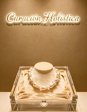 Necklace in a clear box on a beige background with 'Curacion Holistica' text.