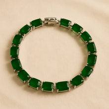 “Handmade sterling silver bracelet with rectangular natural emeralds displayed on a cream stone surface with vibrant Spanish scenery in the background – exclusive boho statement jewelry by Curación Holística.”
