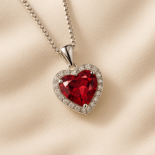 Elegant ruby heart-shaped necklace set in sterling silver with sparkling halo detail, photographed on a cream velvet background, designed by Corazón Holistica in boho statement style.