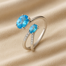 Adjustable sterling silver ring with dual blue topaz stones on luxury cream box