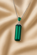“Sterling silver statement necklace with emerald baguette pendant and pear-cut accent, displayed on soft cream satin”
