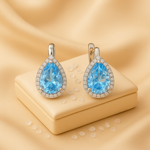 Aquamarine and white quartz teardrop earrings displayed on cream velvet jewelry box