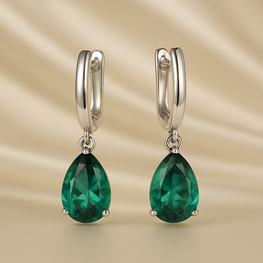 Close-up of sterling silver emerald teardrop earrings on satin cream background