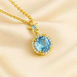 “Elegant gold-plated sterling silver necklace featuring a radiant aquamarine gemstone surrounded by a delicate halo of sparkling stones, displayed on a luxurious cream satin background.”