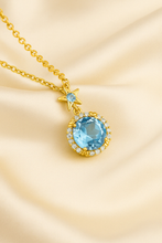 “Elegant gold-plated sterling silver necklace featuring a radiant aquamarine gemstone surrounded by a delicate halo of sparkling stones, displayed on a luxurious cream satin background.”