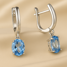Sterling silver hoop earrings with oval-cut aquamarine gemstones on satin gold background — Curación Holística
