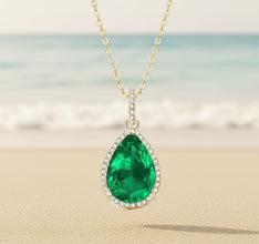 Gold necklace with a green teardrop pendant on a blurred beach background