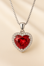 Elegant ruby heart-shaped necklace set in sterling silver with sparkling halo detail, photographed on a cream velvet background, designed by Corazón Holistica in boho statement style.