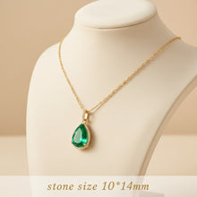 Gold necklace with a green teardrop pendant on a mannequin bust against a beige background.