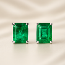 Close-up of radiant emerald green stud earrings on satin cream background