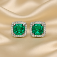 Close-up of emerald halo earrings displayed on satin cream background

